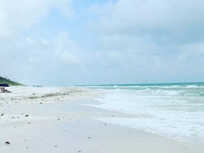 A beach with a clear sky, waves, and a few umbrellas.