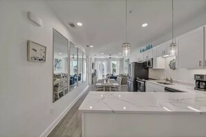 A modern kitchen with a marble island, white cabinetry, and pendant lighting.