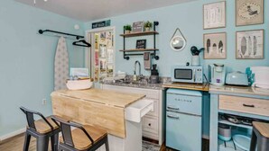 A compact kitchen with a wooden table, a microwave, a coffee maker, and a small refrigerator. - Tiny Home Near the Bay by Beach's, Pensacola, Foley, Gulf Shores, Orange Beach
 (Elberta)