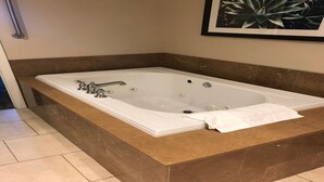 Ein modernes Badezimmer mit einer großen, freistehenden Badewanne, einer Marmorarbeitsplatte und einer gerahmten Pflanze an der Wand.