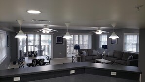 Eine moderne Küche mit dunkler Arbeitsplatte, ein Essbereich mit Tisch und Stühlen sowie ein Wohnbereich mit Sofa und zwei Lampen.
