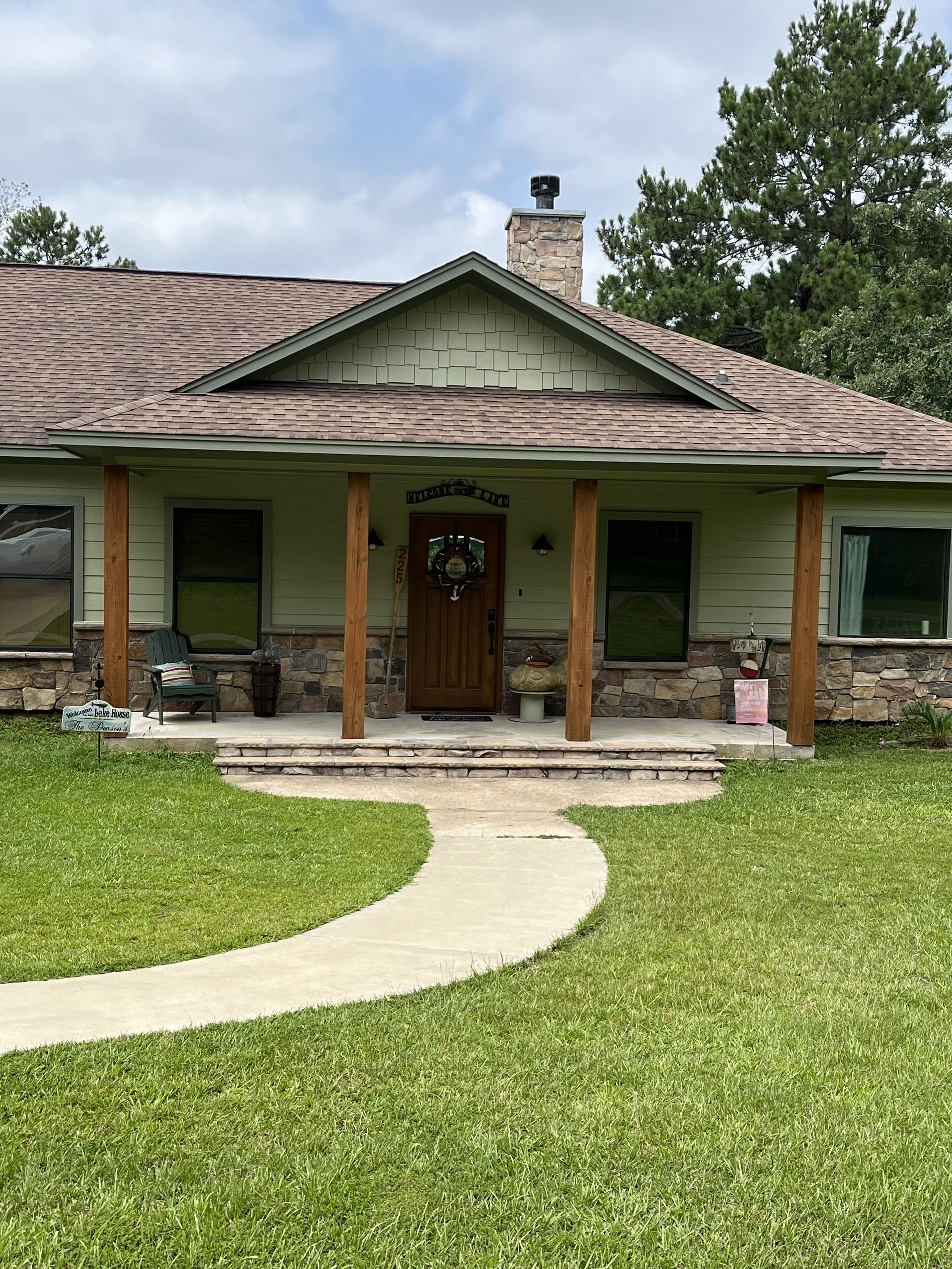A house with a stone chimney, a front porch with wooden posts, a welcome sign, and a mailbox.