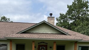 Una casa con chimenea de piedra, un porche con columnas de madera, un cartel de bienvenida y un buzón.