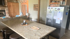 Una cocina con una isla grande, taburetes de bar, un refrigerador y una zona de comedor con un sofá.