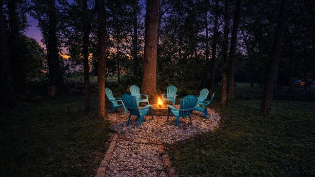 A cozy outdoor seating area with four Adirondack chairs arranged around a fire pit, surrounded by a gravel path and trees. - Midnight Lexington Newly Remodeled Designer Stay (Lexington)