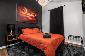 A bedroom with a black and orange color scheme, featuring a bed with a black headboard, a black and gold lamp, and a large painting of a horse on a red background.