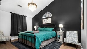 A bedroom with a black and white color scheme, a bed with teal bedding, two bedside tables with lamps, a chair, and a chandelier. - Midnight Lexington Newly Remodeled Designer Stay (Lexington)