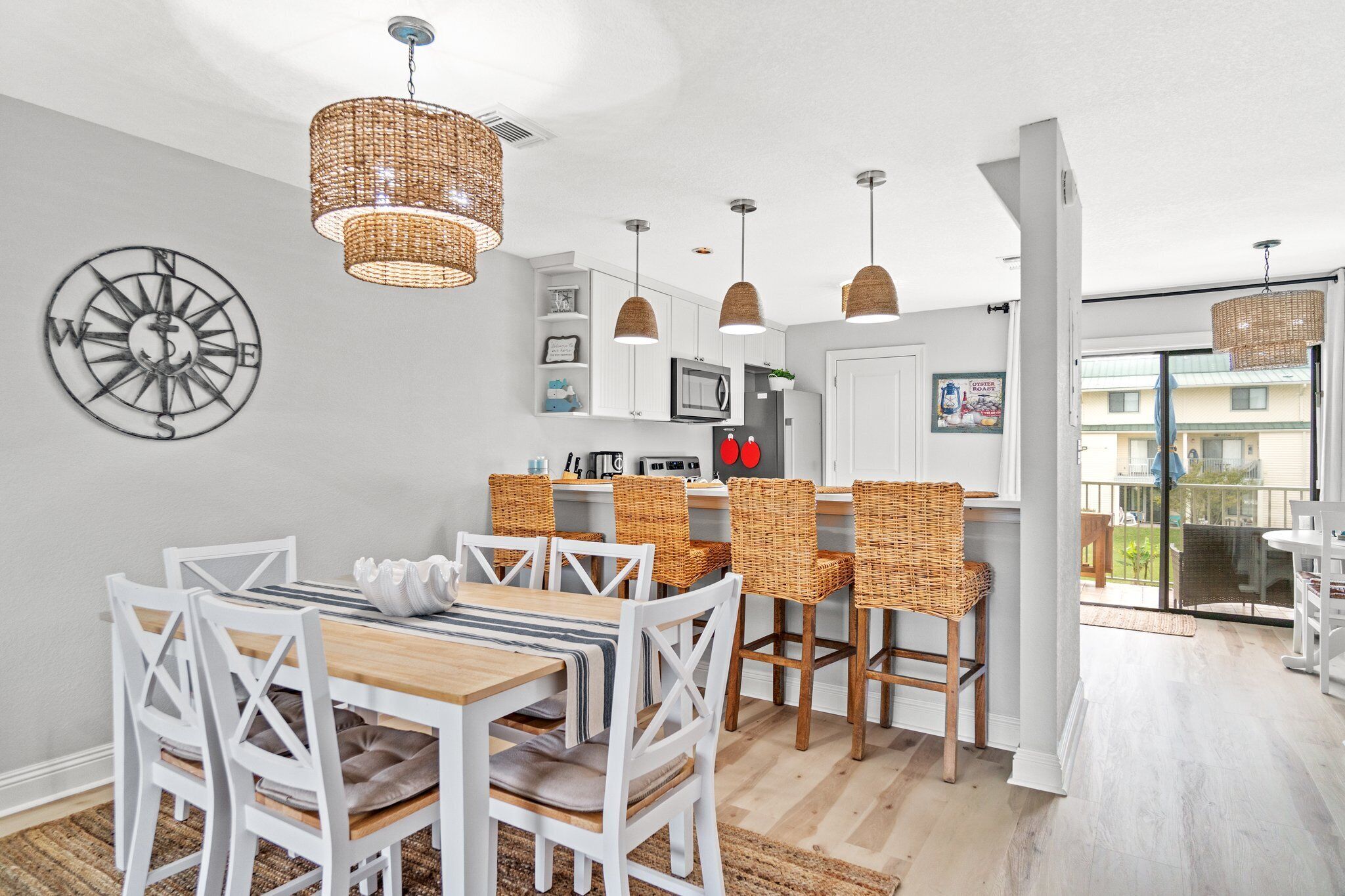 A modern kitchen with white cabinetry, a dining area with white chairs, and a large window overlooking a balcony.