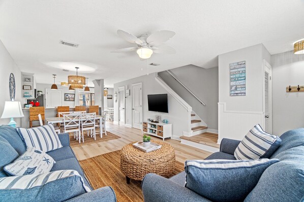 A modern living room with a sofa, ottoman, and a dining area with chairs and a table. - Steps to beach Pool Parking 2 king beds beach gear Patio WI-FI (Miramar Beach)