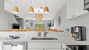 A modern kitchen with white cabinetry, a stainless steel sink, a dishwasher, and a stove. There are wicker baskets on the countertop and a coffee maker. - Steps to beach Pool Parking 2 king beds beach gear Patio WI-FI (Miramar Beach)