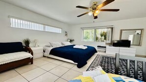 A bedroom with a bed, a sofa, a TV, a ceiling fan, and a window. - Beach Tide Motel - #5 Studio 1 King bed (Hollywood)