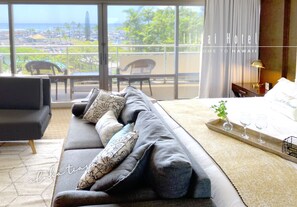 Relax in this serene hotel room with a view of the resort area, featuring a comfortable bed and stylish seating area.