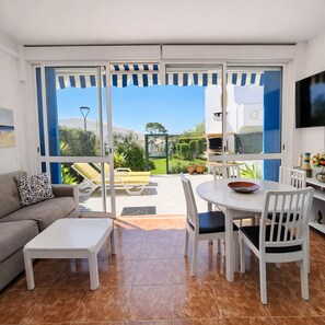 A living room with a sofa, coffee table, dining table, chairs, and a TV.