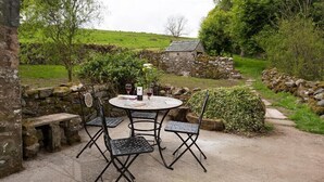 Une table en pierre avec quatre chaises, une bouteille de vin et un menu, le tout installé dans un cadre champêtre en plein air.