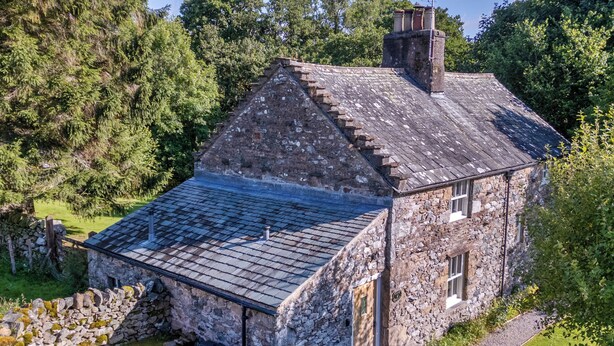 Une maison en pierre avec un toit en pente, un mur en pierre et un petit porche.
