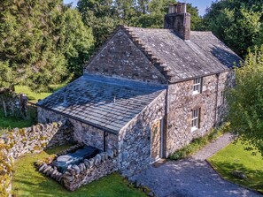 A stone house with a sloped roof, a stone wall, and a small porch. - Lacet Cottage (Penrith)