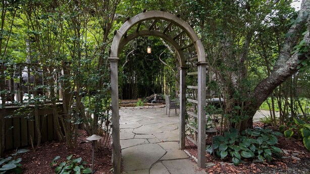 A stone pathway leading through a wooden archway surrounded by lush greenery and trees. - New Pool Lovely Home Mins away from Town & Beach (Nantucket)