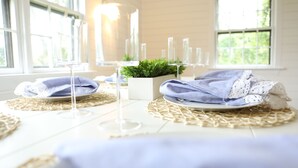 A dining area with a table set for two, featuring clear glassware, a small potted plant, and a lace table runner. - New Pool Lovely Home Mins away from Town & Beach (Nantucket)