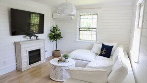 A living room with a fireplace, white furniture, a television, and a large window. - New Pool Lovely Home Mins away from Town & Beach (Nantucket)