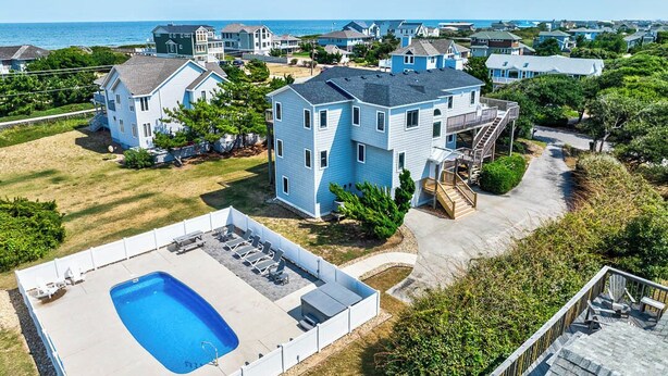 A large two-story house with a swimming pool, surrounded by other houses and a view of the ocean.