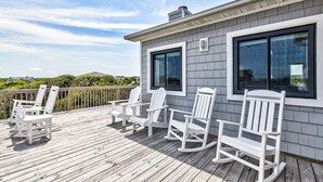 A wooden deck with white rocking chairs and a building with large windows.