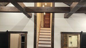 A staircase with wooden beams, a white door at the top, and a bathroom with a bathtub and sink.