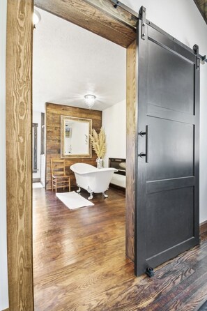 A modern bathroom with a wooden floor, a white freestanding bathtub, a wooden chair, and a large mirror on the wall. - Newly renovated early 1900’s farmhouse (Birch Tree)