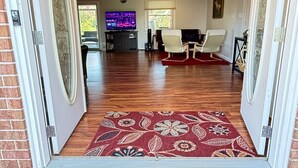 A spacious living room with a television, a fireplace, and a red doormat with "Welcome" written on it. - Water front, river views, fishing from backyard, Large yard to enjoy. (Hampton)