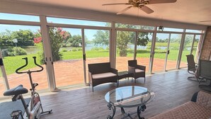A spacious room with a large sliding glass door leading to a patio, a ceiling fan, a glass table, and a seating area with a couch and chairs. - Water front, river views, fishing from backyard, Large yard to enjoy. (Hampton)
