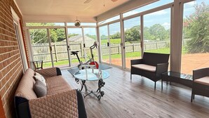 A covered patio with a glass table, a sofa, and two chairs. - Water front, river views, fishing from backyard, Large yard to enjoy. (Hampton)