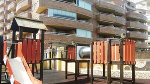 Un'area giochi con scivolo e strutture per arrampicarsi, con sullo sfondo un condominio a più piani dotato di balconi.