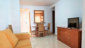 Un soggiorno con un divano, un tavolo da pranzo con sedie, una TV su un mobile in legno e una porta che dà su un'altra stanza.
