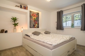 Une chambre à coucher avec un lit, une plante en pot, un tableau et une fenêtre avec des rideaux.