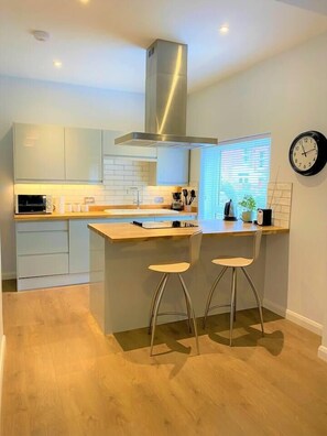 Une cuisine moderne avec un îlot central, des tabourets de bar et une horloge au mur.