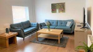 En moderne stue med en sofasæt, et sofabord, et fjernsyn og et lille bord med en lampe.