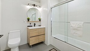 Ein modernes Badezimmer mit Toilette in Weiß, Holzwaschtisch, rundem Spiegel und einer Duschkabine.