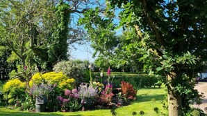 A well-maintained garden with various flowering plants and a neatly trimmed lawn. - Paddock Cottage - Thorpe Arnold, Melton Mowbray (Melton Mowbray)