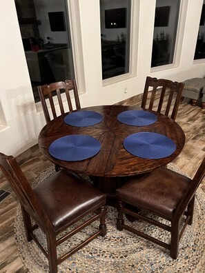 Ein runder Holztisch mit vier blauen Platzsets, umgeben von vier Holzsesseln mit gepolsterten Sitzen.