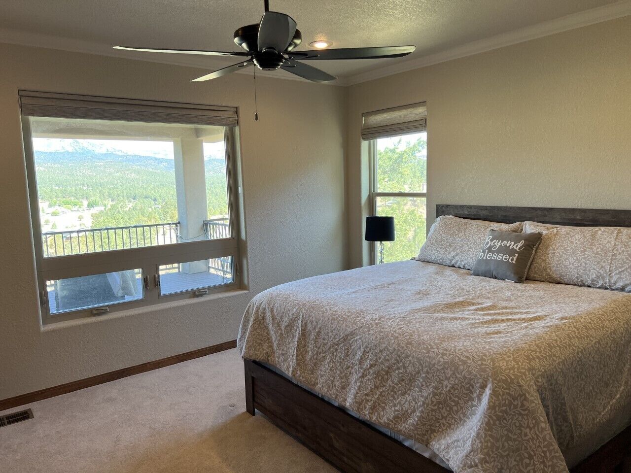 Une chambre dotée d’un grand lit, d’un ventilateur de plafond et de deux fenêtres donnant sur un paysage montagneux.