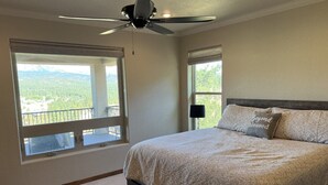 Ein Schlafzimmer mit einem großen Bett, einem Deckenventilator und zwei Fenstern mit Blick auf eine gebirgige Landschaft.