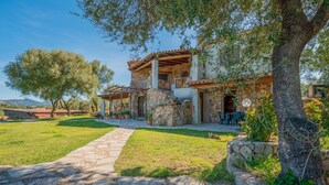 A stone house with a balcony, a paved pathway, and a grassy yard.