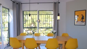 Ein Essbereich mit einem langen Tisch, gelben Stühlen und Blick durch ein Fenster mit einem grünen Tor.