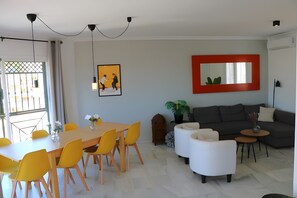 Un salon moderne comprenant un coin repas, un canapé gris et un miroir à cadre rouge.
