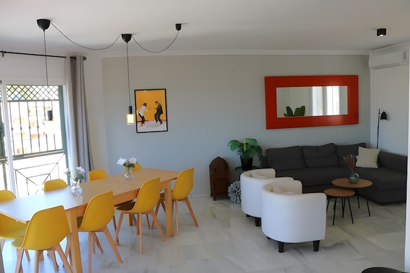 A modern living room with a dining area, a gray sofa, and a red-framed mirror.