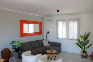 A modern living room with a grey sofa, white armchairs, a small round table, and a large potted plant.