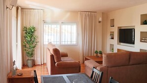 Een woonkamer met een bank, een televisie, een plant en een raam met gordijnen.