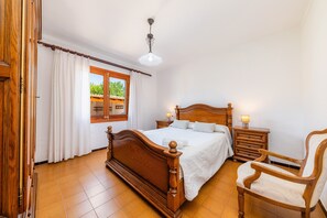Un dormitorio con una cama de madera, mesitas de noche, una silla, una ventana con cortinas y una lámpara en el techo.