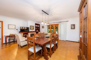 A dining area with a wooden table and chairs, a television, and a kitchen area with a counter and cabinets. - Country House "La Sort Den Jaume" with Mountain View, Private Pool & Wi-Fi (Pollença)