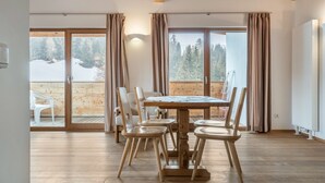 Ein Holztisch mit Stühlen, eine Schiebetür zu einem verschneiten Außenbereich und eine Holzbalkendecke.