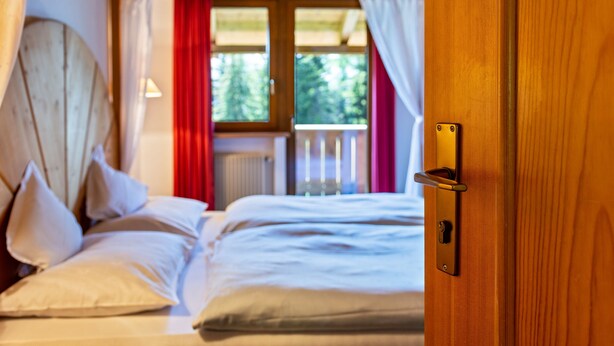 Quarto com cama, janela com cortinas e porta de madeira.